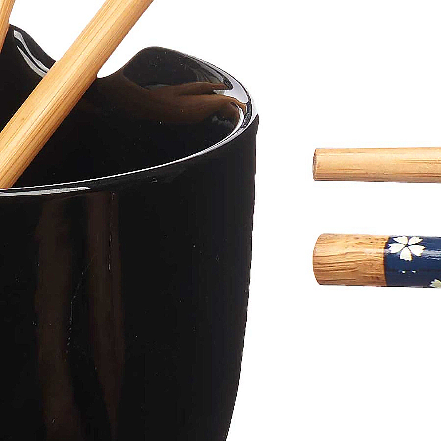 Contenitore in ceramica nero con bacchette. Due bacchette sono all'interno. Due sono sul lato destro. Uno è decorato.