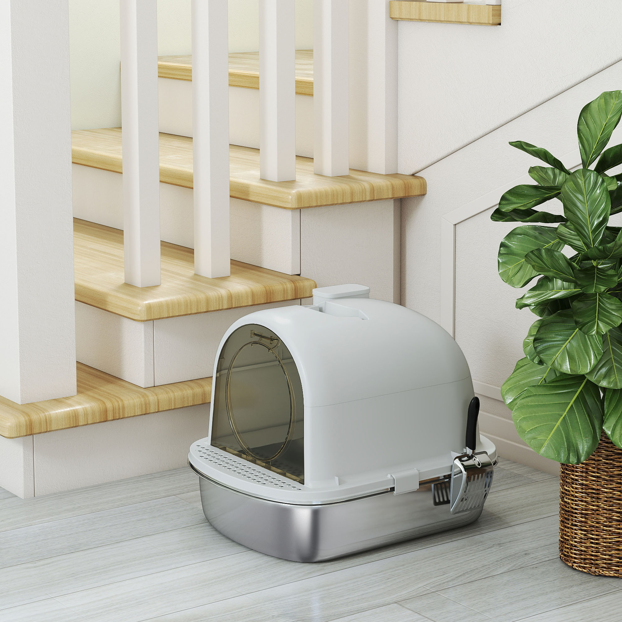 Una caja de arena para gatos cerca de unas escaleras y una planta. La caja es blanca y plateada.