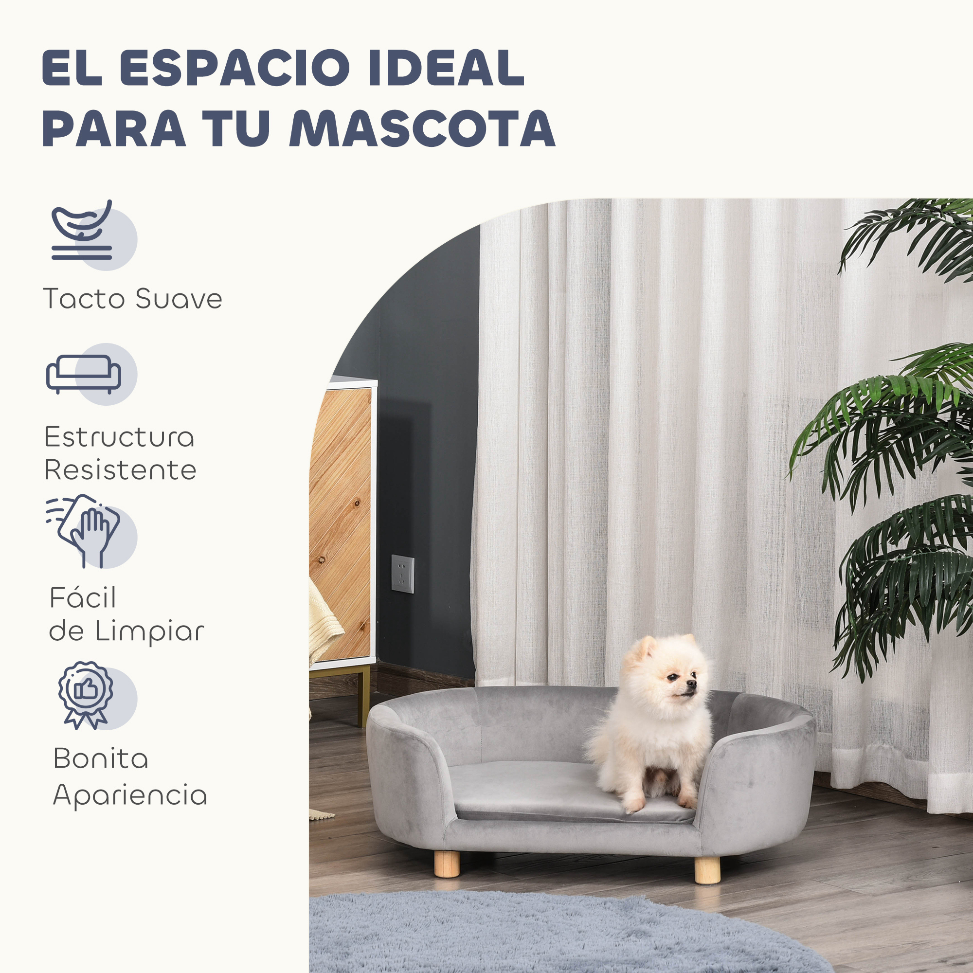 Un perro pequeño está sentado en una cama gris para mascotas. El fondo tiene una cortina blanca y una planta.