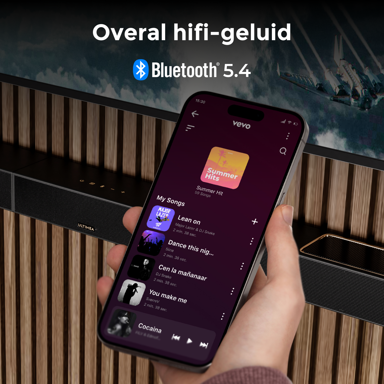 A hand holds a phone playing music. A soundbar is below it. The background has a wooden wall and a screen.