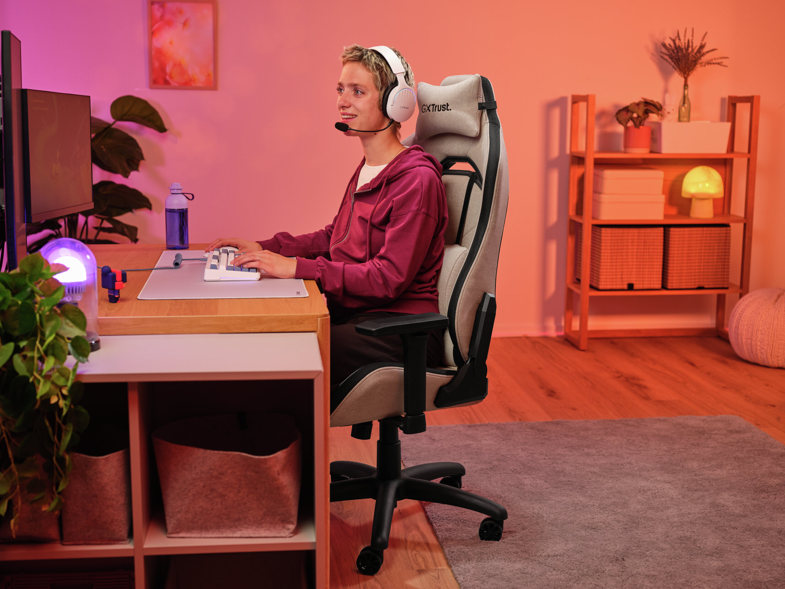 Osoba z zestawem słuchawkowym siedzi przy biurku z monitorem, pisząc na klawiaturze, w konfiguracji do gier.