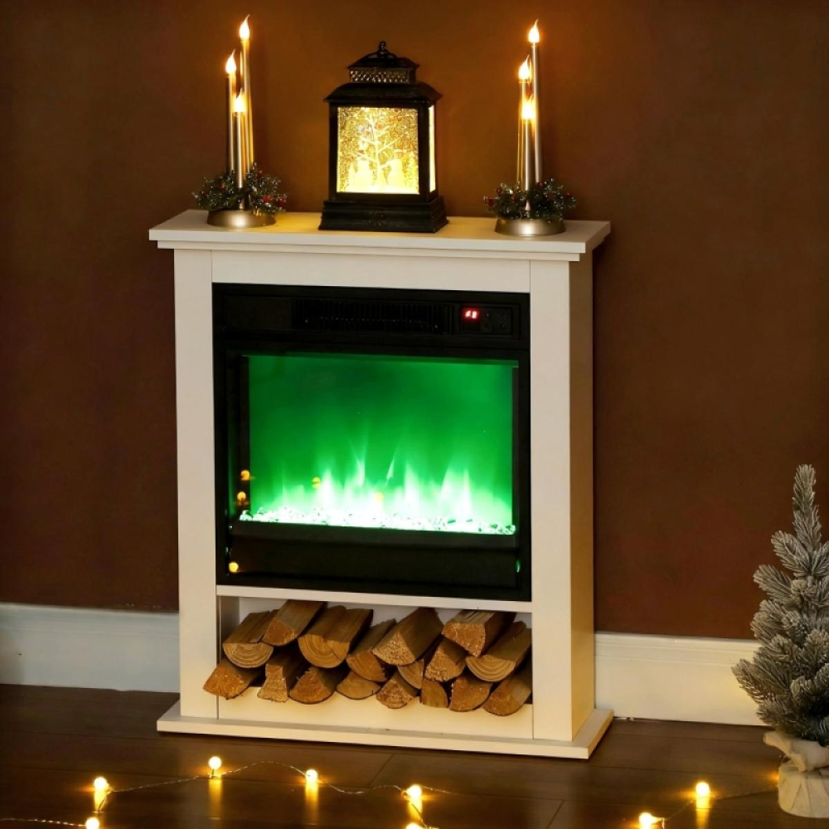 Weißer Kamin mit grünen Flammen, Kerzen und Laterne. Holzscheite im Regal darunter. Kleiner Weihnachtsbaum rechts.