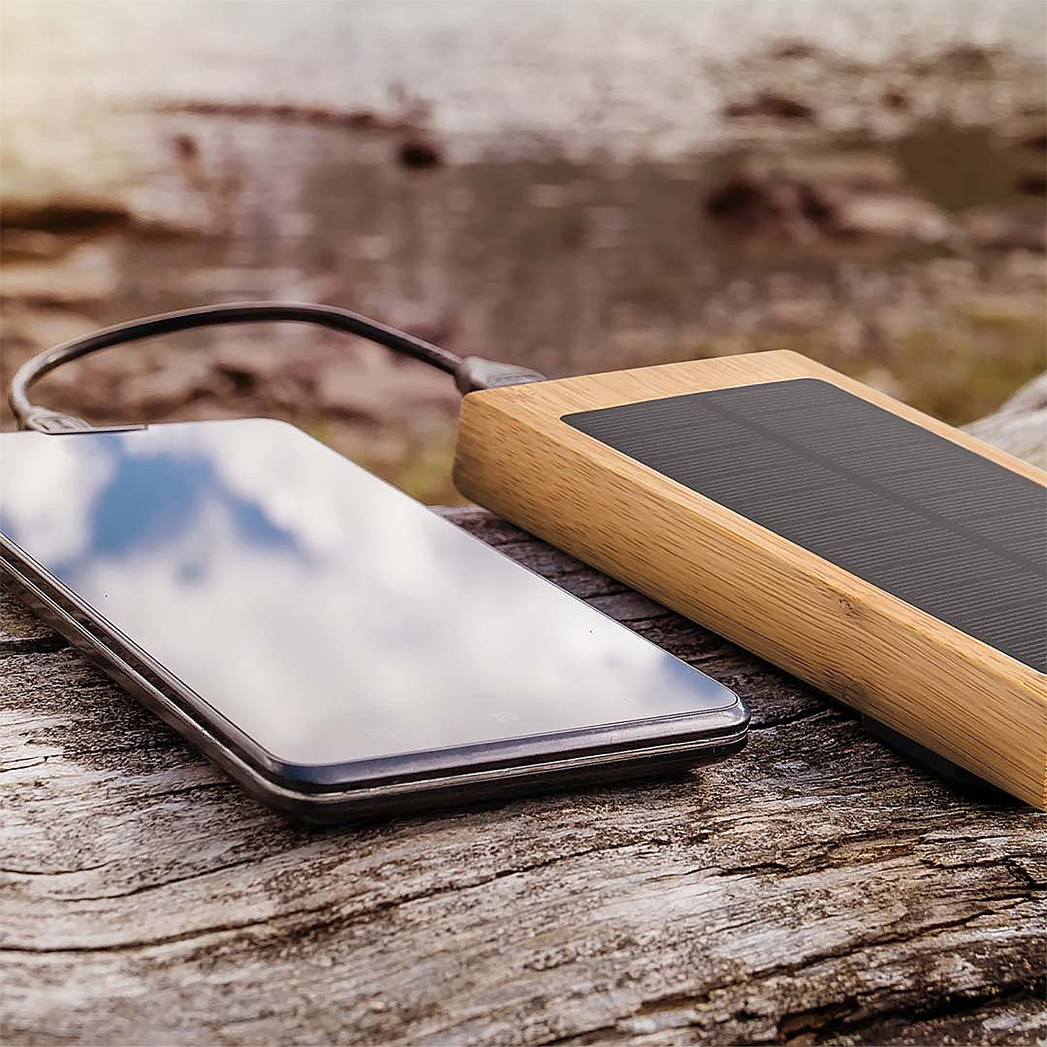 Uno smartphone collegato a un power bank solare con cornice in legno. Entrambi i dispositivi sono su una superficie in legno.