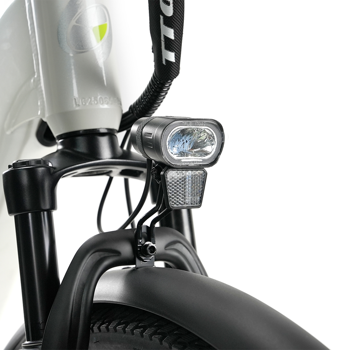 Zbliżenie przodu roweru. Reflektor i odblask są zamontowane na czarnej ramie. Rower jest biało-czarny.