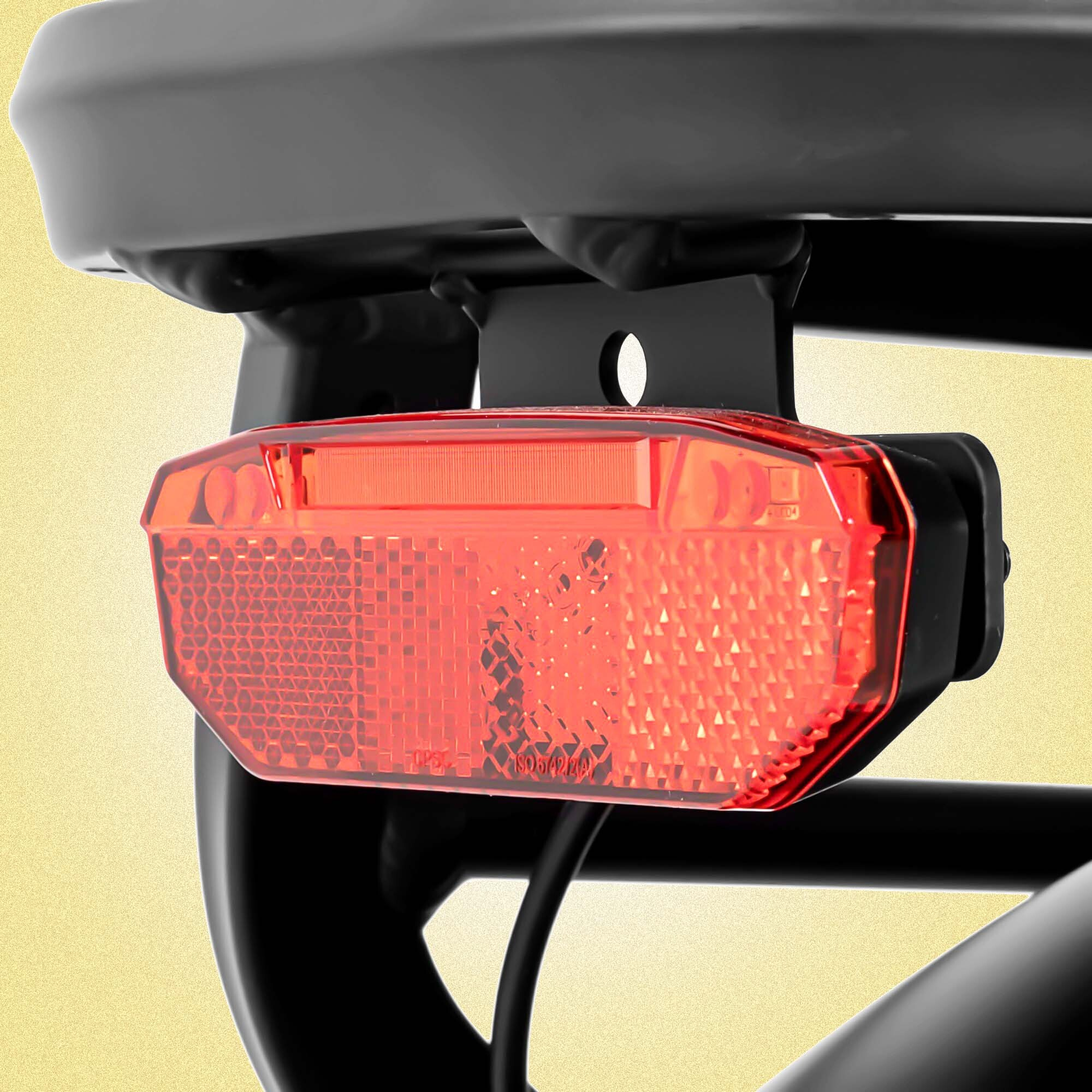 Zbliżenie czerwonego odblasku przymocowanego do czarnej metalowej ramy. Odbłyśnik jest prostokątny z teksturowaną powierzchnią.