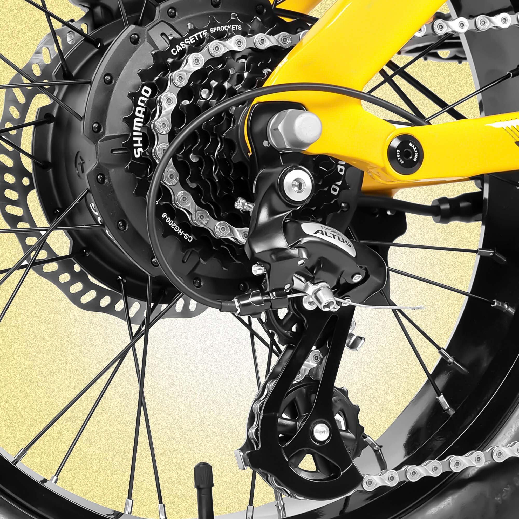 Zbliżenie koła roweru z żółtą ramą, czarnymi zębatkami, łańcuchem i przerzutką Shimano Altus.