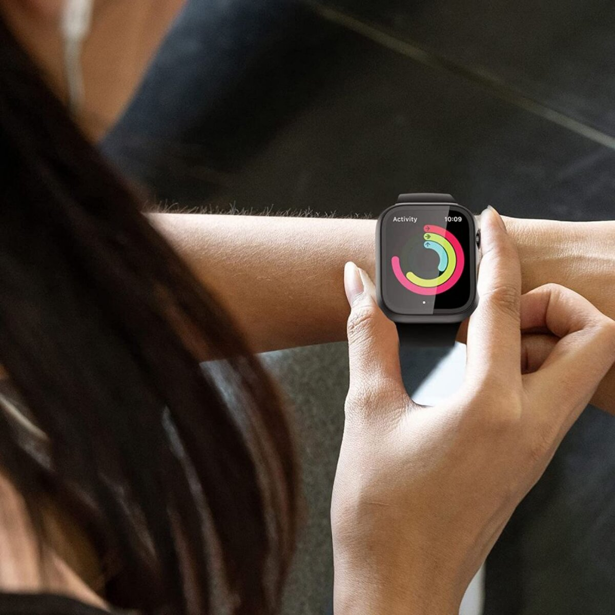 Une personne portant une montre intelligente, affichant des anneaux d'activité. La montre est au poignet, l'heure est visible. L'arrière-plan est flou.