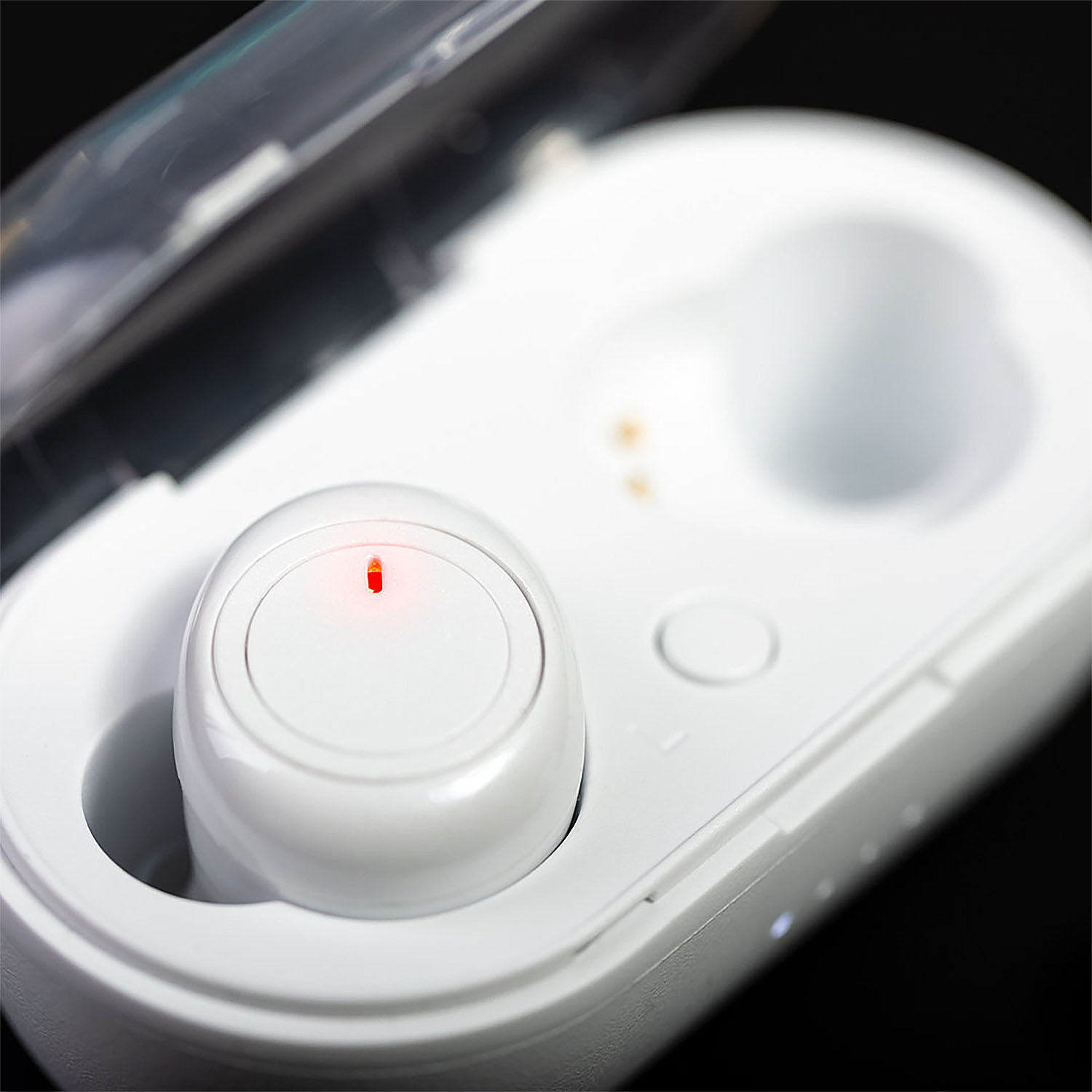 Un auricolare bianco dentro la sua custodia di ricarica. L'auricolare ha una luce rossa. La custodia è aperta, su sfondo nero.