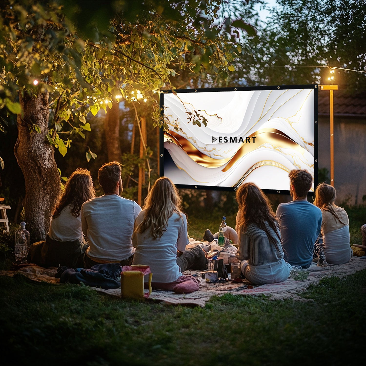 Gruppe schaut im Freien einen Film auf einer Leinwand mit goldenem Design. Sie sitzen auf einer Decke unter einem Baum mit Lichtern.