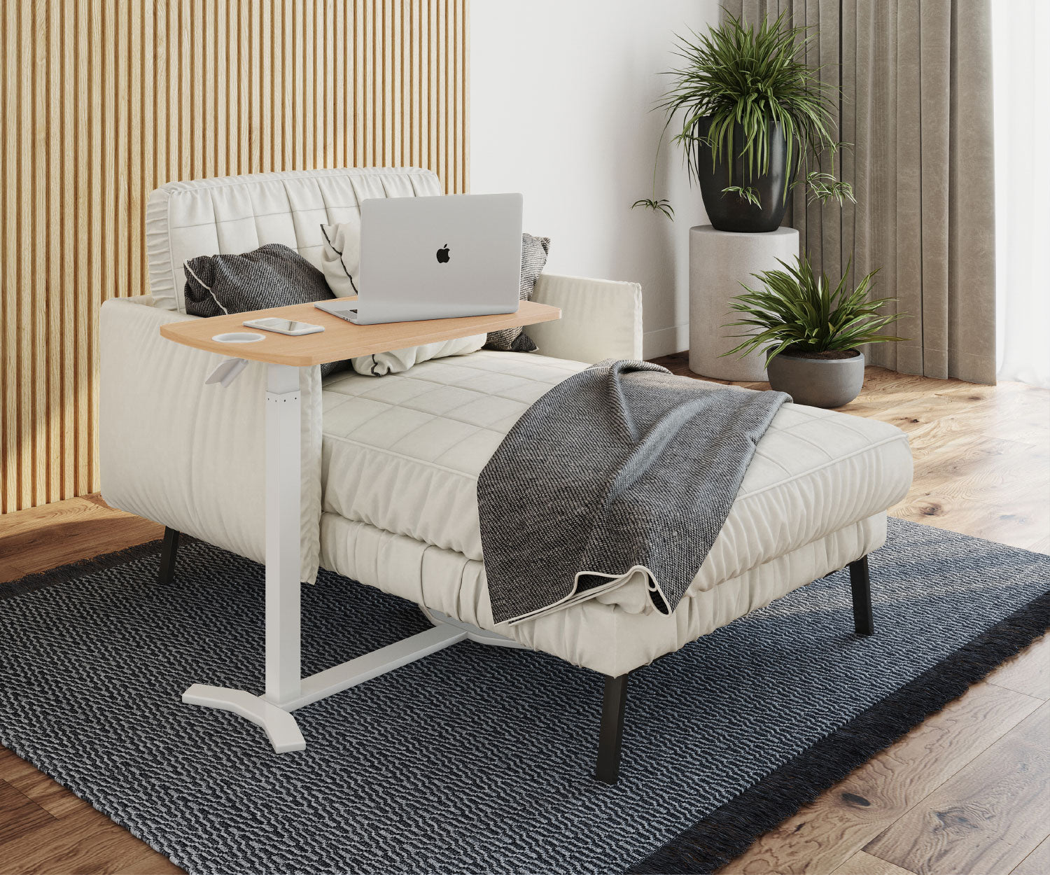 Ein Laptop steht auf einem Holztisch neben einer Couch. Pflanzen sind im Hintergrund. Eine Decke bedeckt einen Teil der Couch. Teppich.