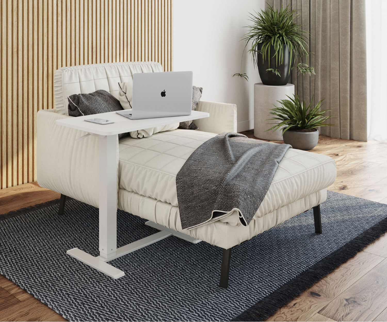 Ein weißer Laptop steht auf einem Tisch über einer weißen Chaiselongue. Pflanzen und ein Teppich sind im Hintergrund.