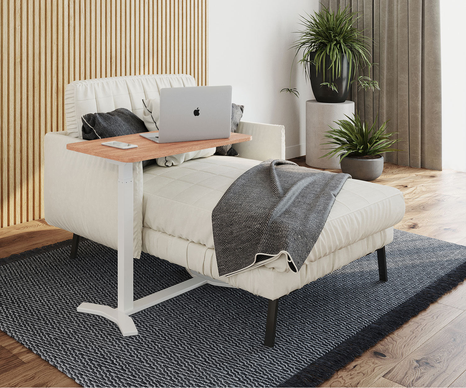 Ein Laptop auf einem Holztisch neben einem weißen Sofa. Pflanzen in Töpfen sind im Hintergrund. Ein Teppich liegt auf dem Holzboden.