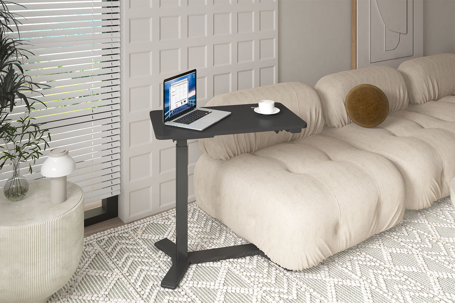 Ein Laptop auf einem schwarzen Tisch steht neben einem beigen Sofa, eine weiße Tasse auf dem Tisch. Links ein Fenster mit Jalousien und ein runder Tisch.