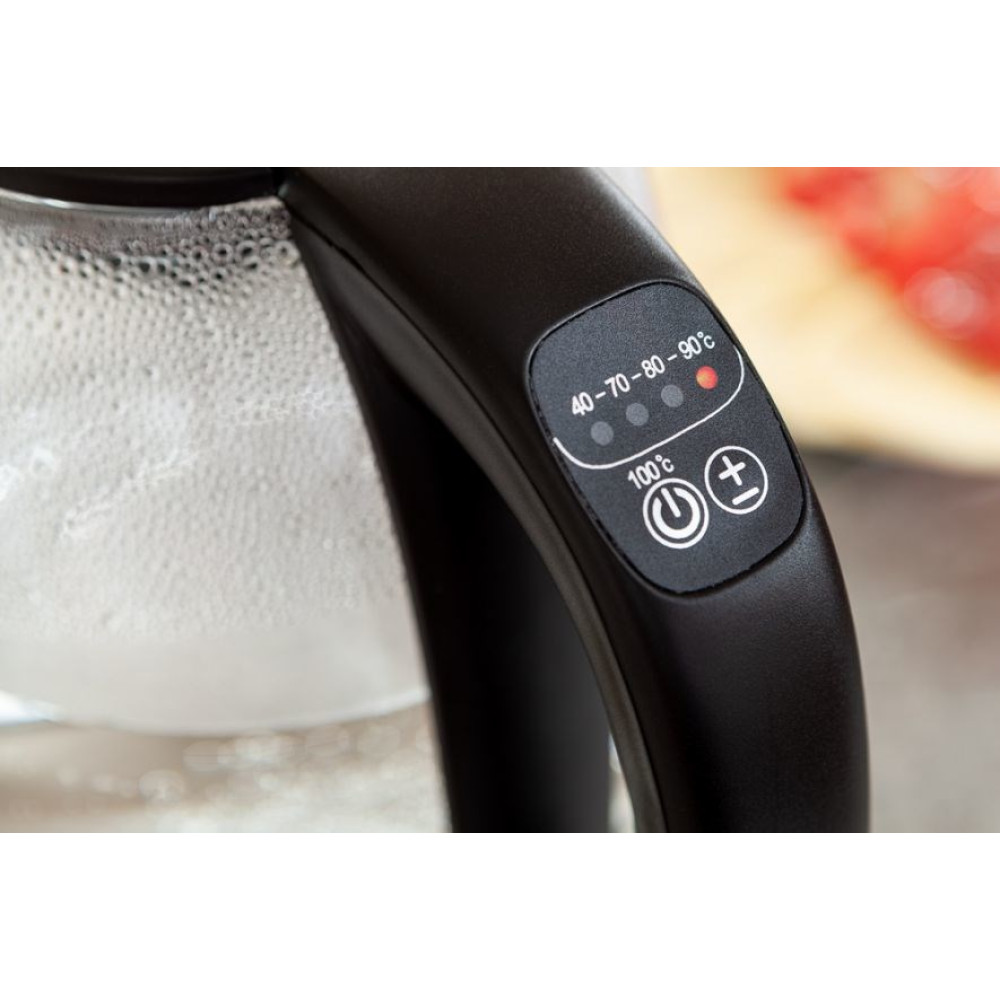 Zbliżenie czarnego uchwytu czajnika elektrycznego z regulatorami temperatury. Czajnik jest częściowo widoczny, z parą w środku.