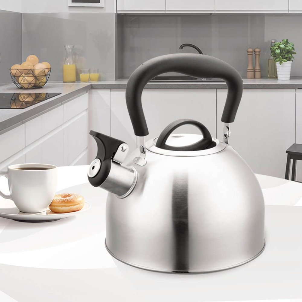 Un bollitore in acciaio inossidabile con manico nero è su un tavolo bianco. Una tazza di caffè e una ciambella a sinistra.