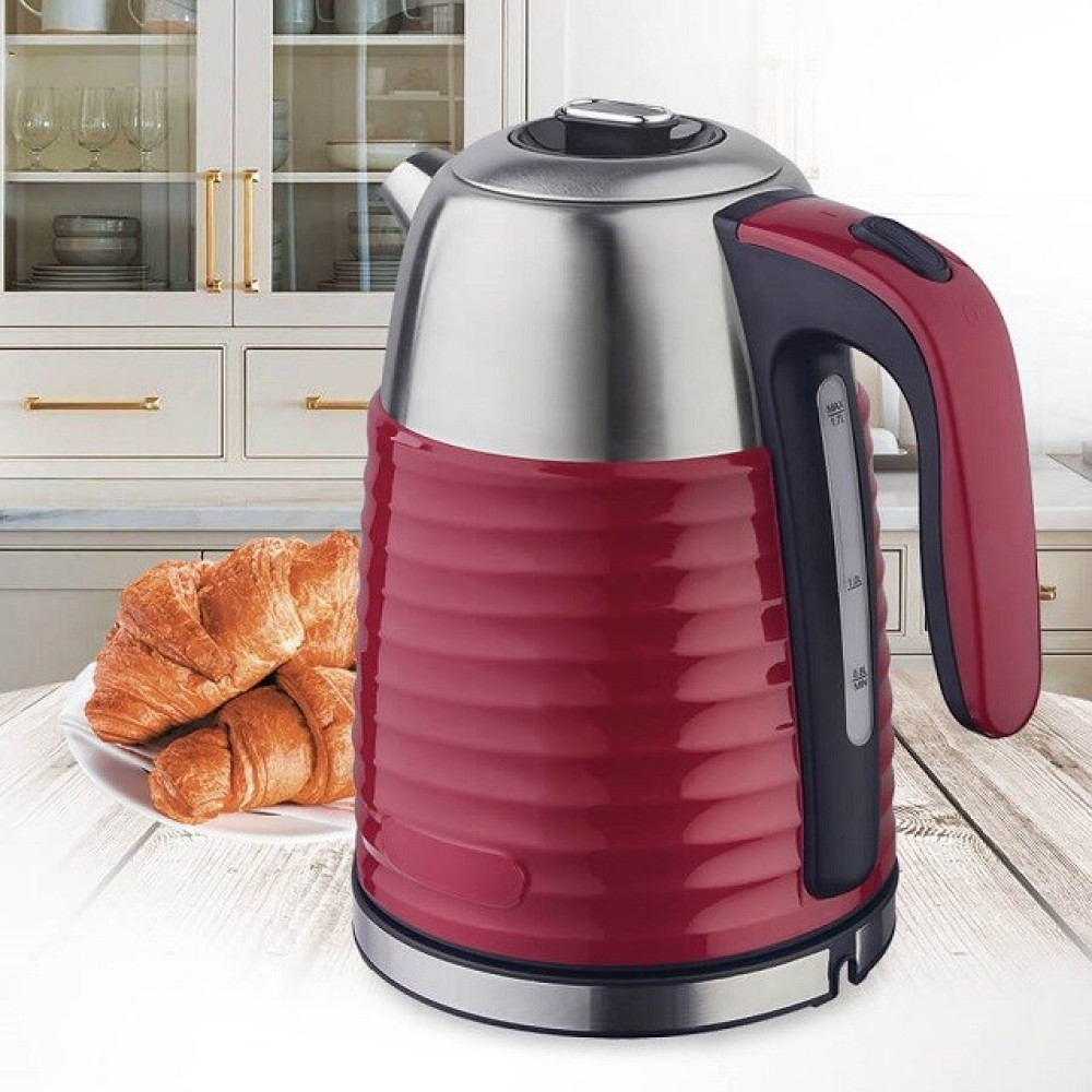 Bollitore elettrico rosso e argento su un tavolo di legno, croissant su un piatto davanti. Mobili da cucina sullo sfondo.