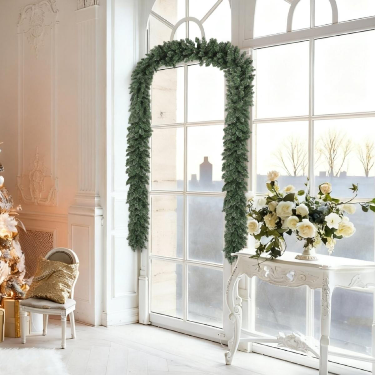 Ein Raum mit großen Fenstern, geschmückt mit einer grünen Girlande. Es gibt einen Tisch mit Blumen. Links steht ein Stuhl mit einem goldenen Kissen.