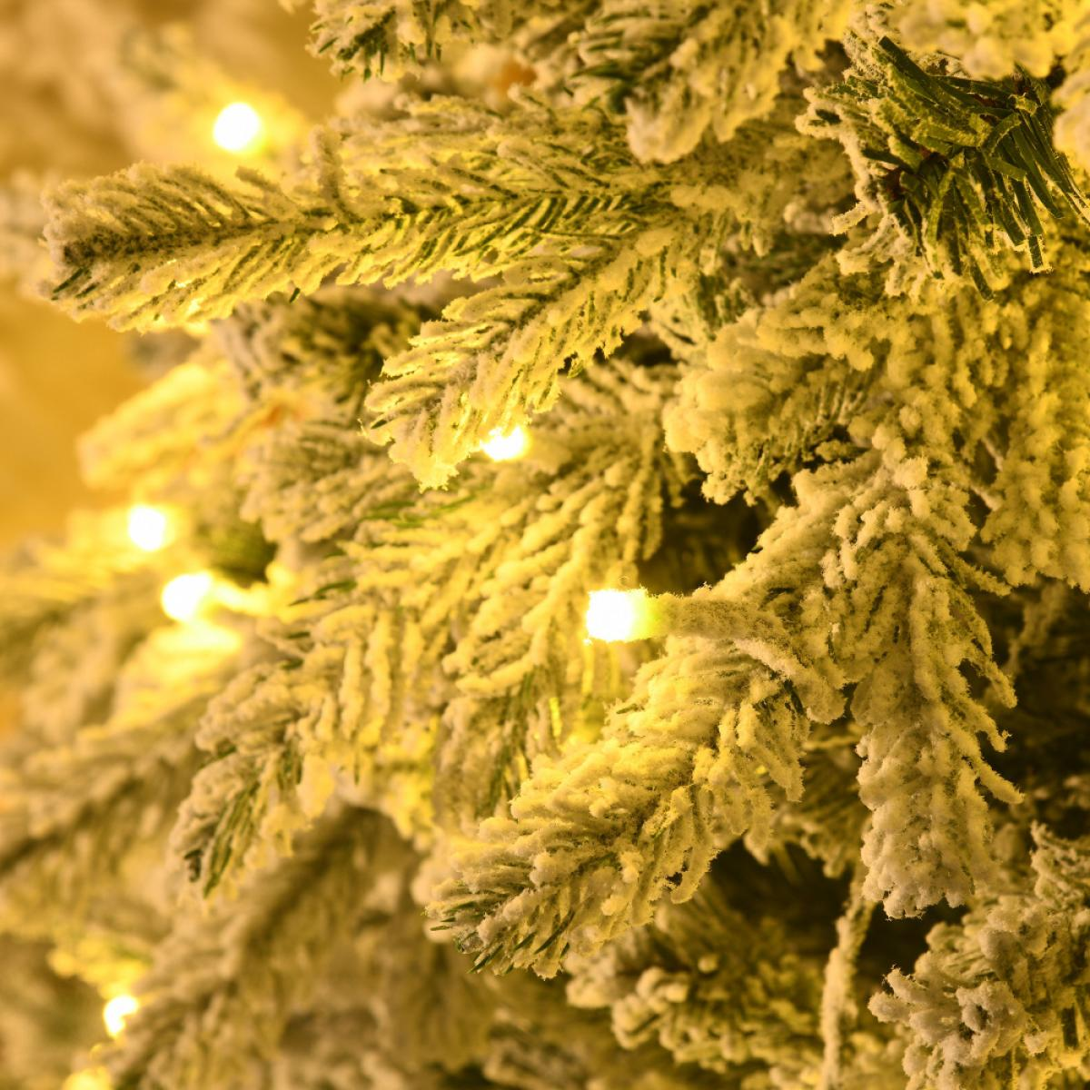 Nahaufnahme eines schneebedeckten Weihnachtsbaums mit hellgelben Lichtern. Die Nadeln sind grün, mit weißem Schnee und einigen Lichtern.