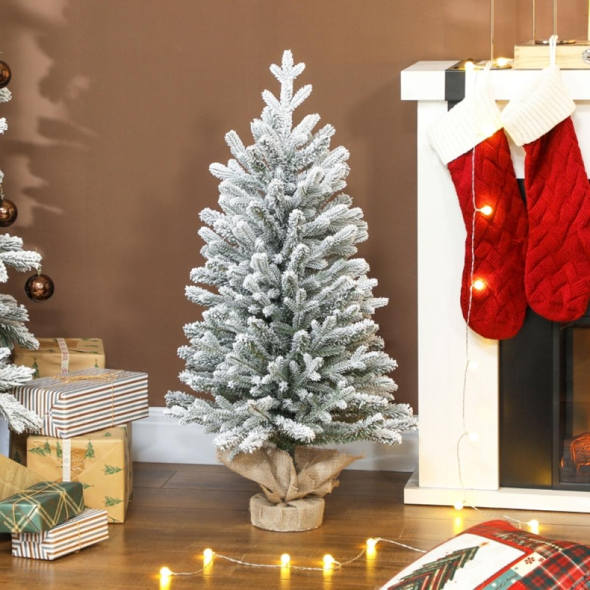 Ein geschmückter Weihnachtsbaum steht vor einem Kamin mit roten Strümpfen. Geschenke liegen unter dem Baum, und Lichterketten liegen auf dem Boden.