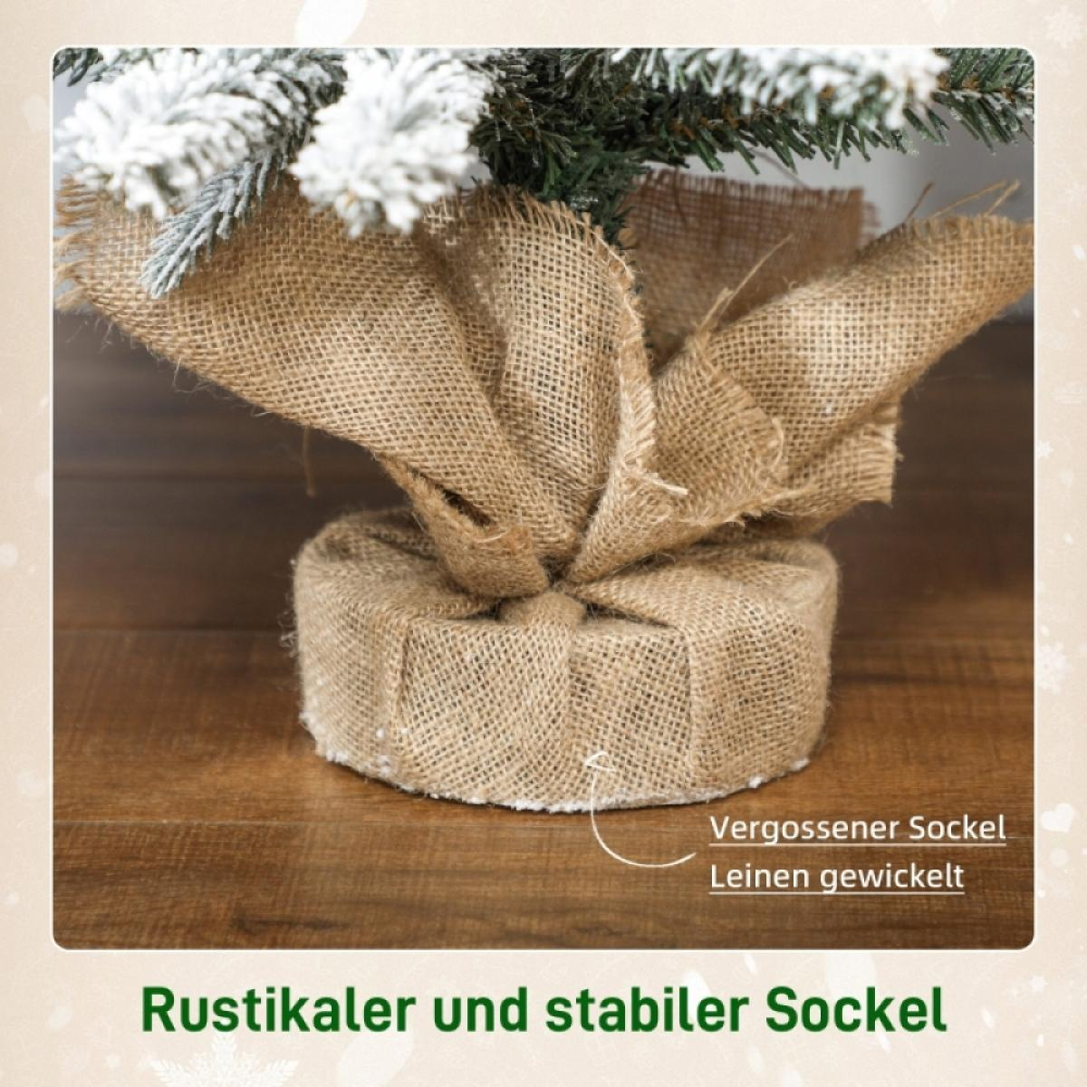 Ein kleiner Weihnachtsbaumfuß ist in Jute gewickelt. Die Baumspitze hat weiße Akzente. Der Sockel steht auf einer Holzoberfläche.
