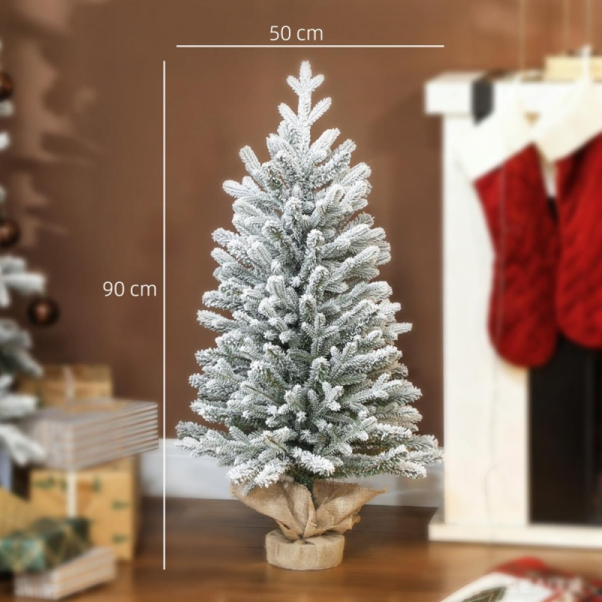 Ein kleiner, schneebedeckter Weihnachtsbaum vor einem Kamin mit roten Strümpfen. Ein Holzboden vervollständigt die Szene.