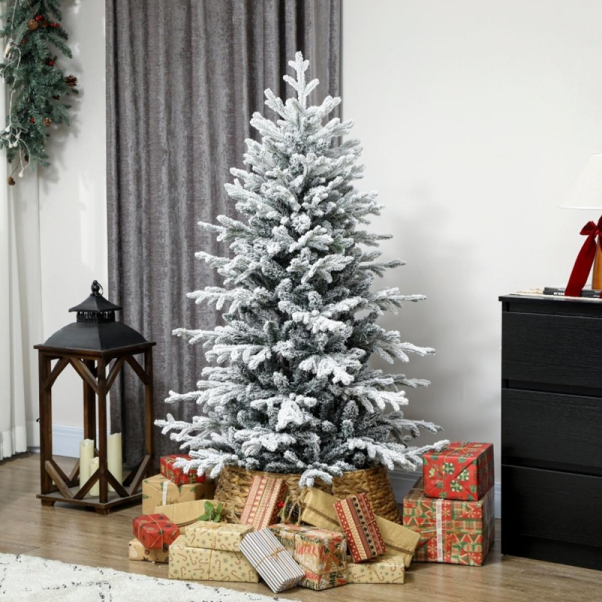 Ein geschmückter Weihnachtsbaum mit Geschenken darunter. Auf beiden Seiten stehen eine Holzlaterne und eine schwarze Kommode. Links hängt eine Girlande.