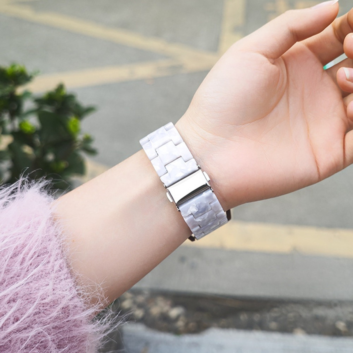 Polso di una persona con un orologio di marmo bianco. È visibile una manica rosa. Lo sfondo è una scena stradale sfocata.