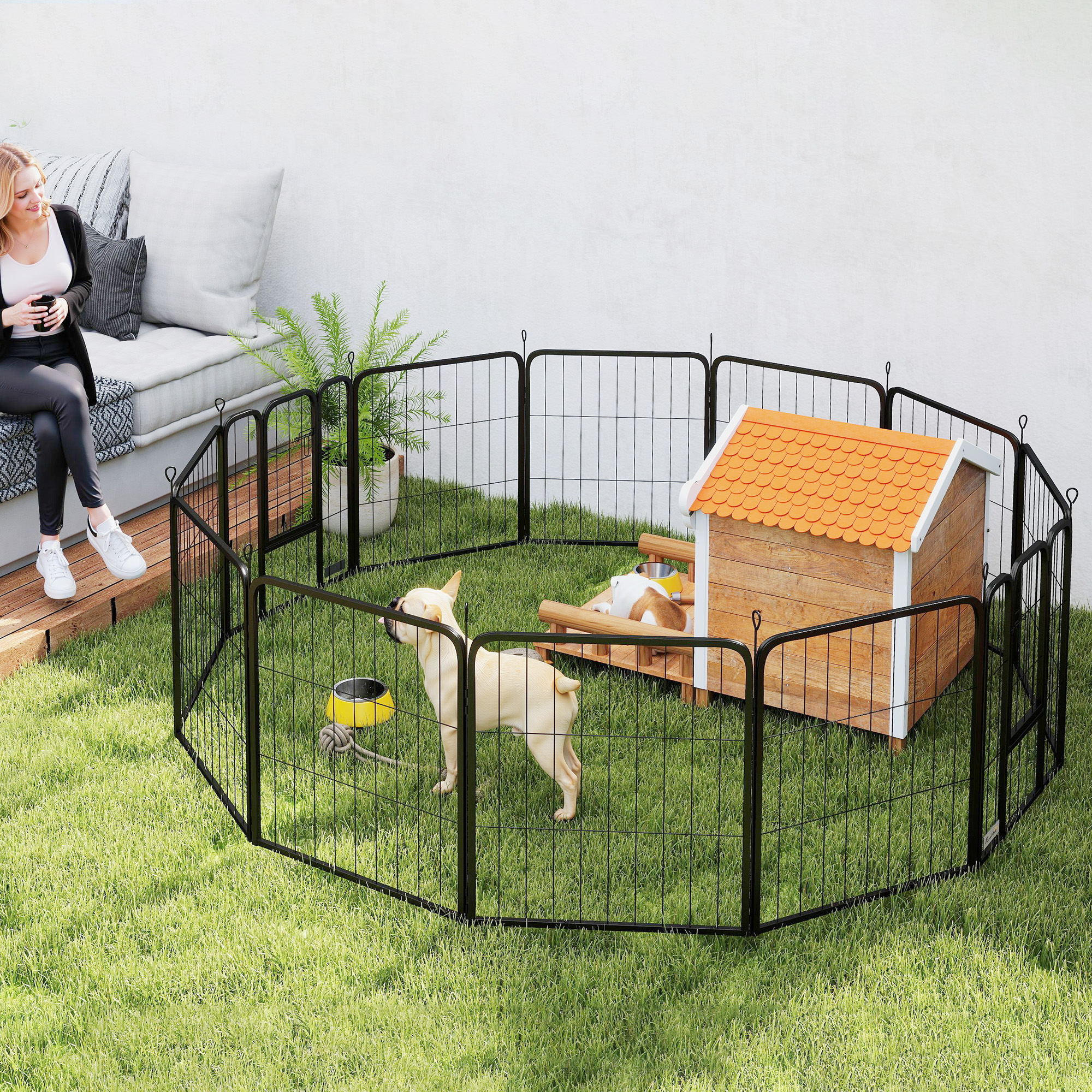 Una mujer sentada cerca de un corral para perros con un perro y una caseta. El corral está sobre césped.