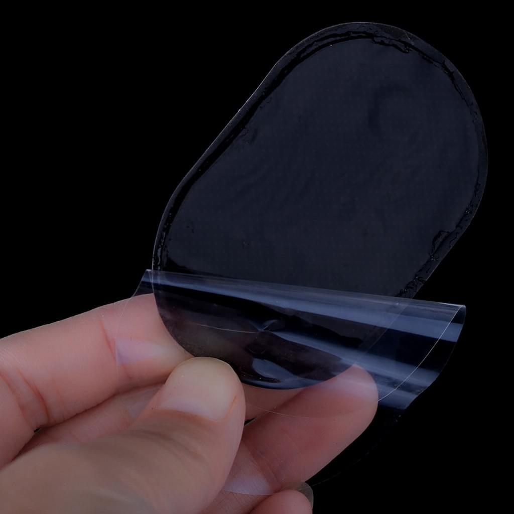 Eine Hand hält ein schwarzes, oval geformtes Klebepad mit einer sich ablösenden transparenten Folie vor schwarzem Hintergrund.