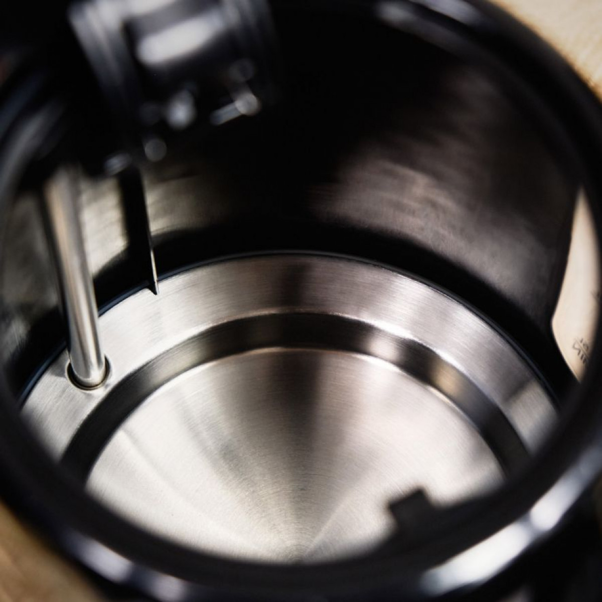 Widok wewnątrz czajnika ze stali nierdzewnej. Wewnątrz widoczna metalowa rurka. Czajnik jest czarny ze srebrnym wnętrzem.