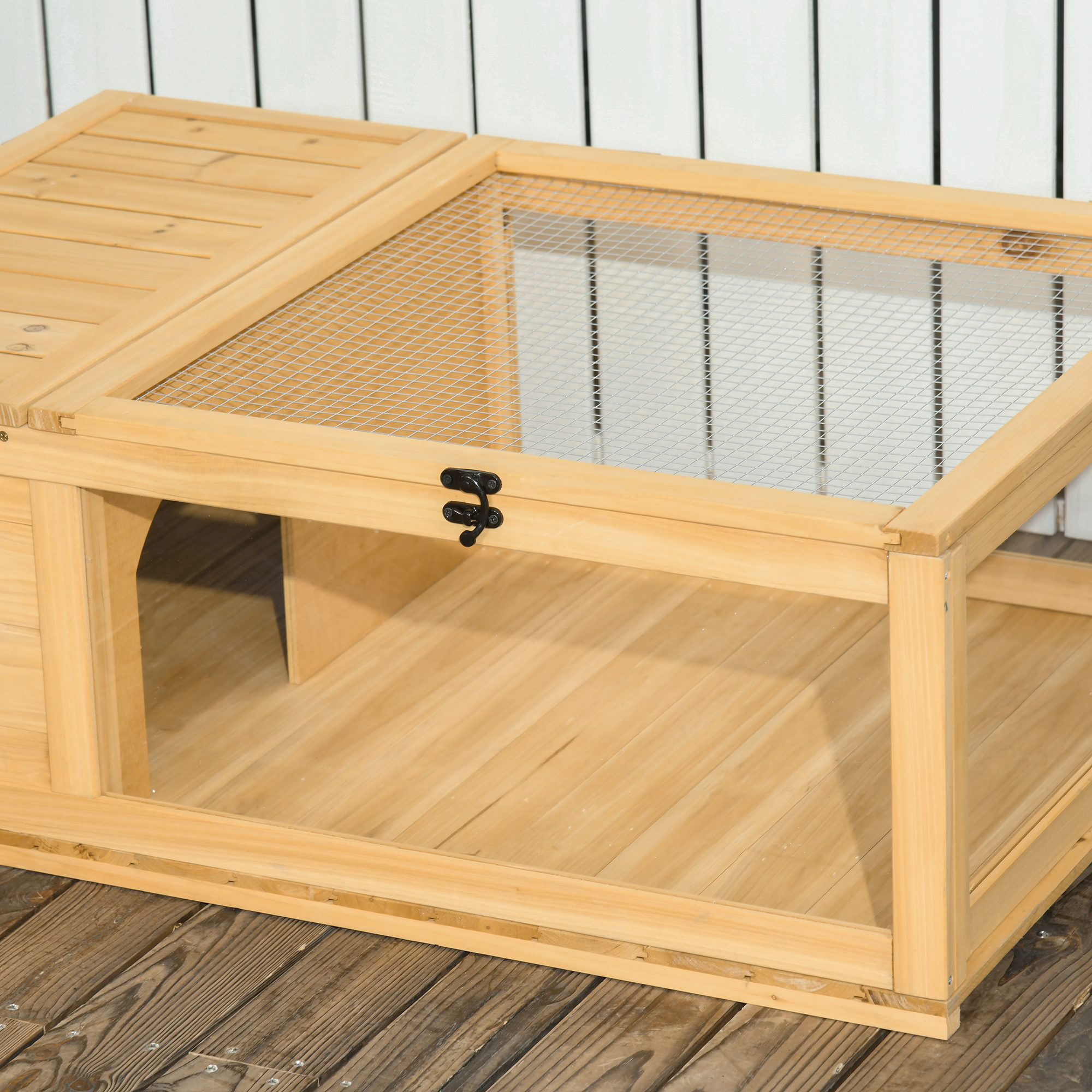 Jaula de madera para animales pequeños con techo de malla, puerta y suelo de madera, contra una pared blanca y un suelo de madera.