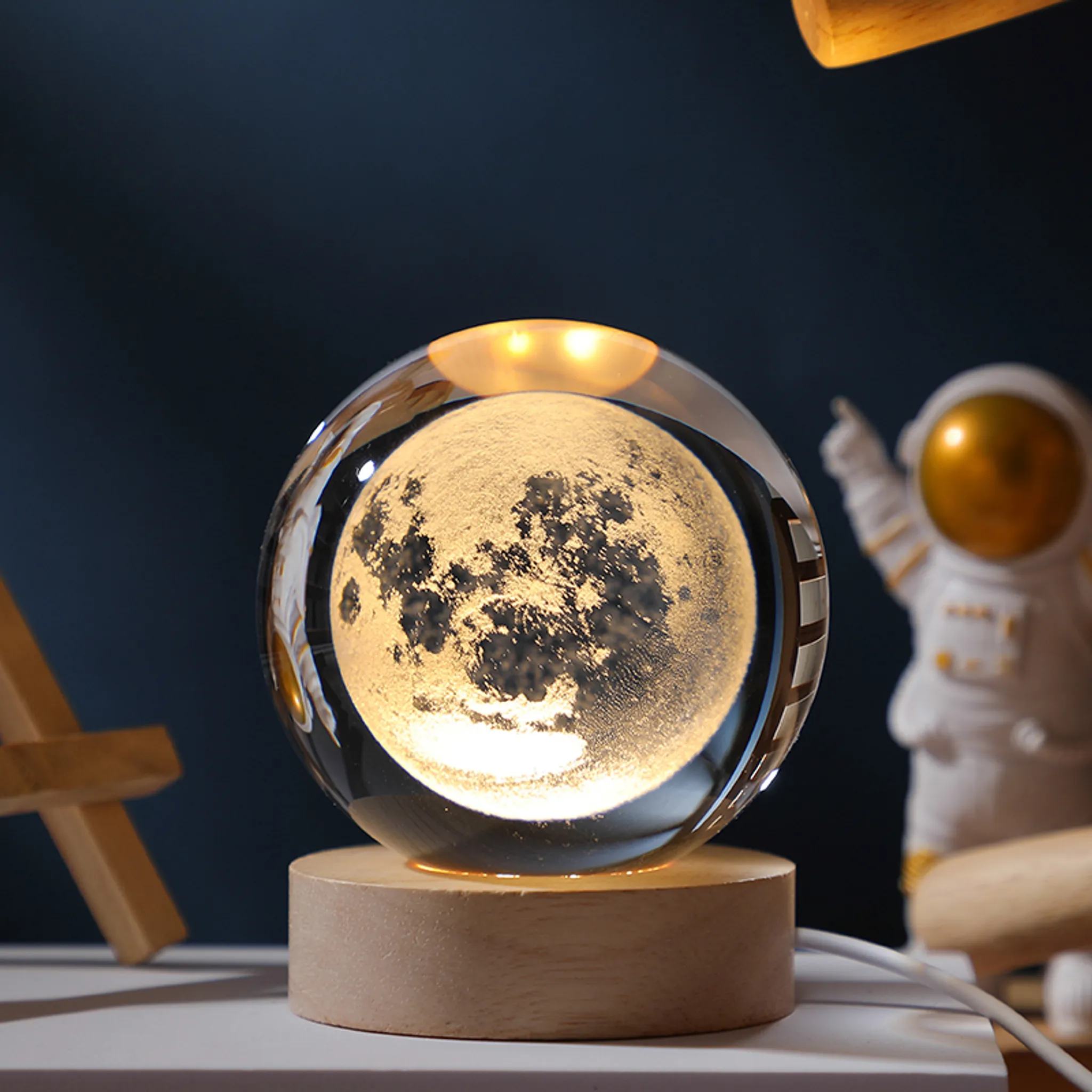 Eine Kristallkugel mit Mond, auf Holzsockel. Astronautenfigur zeigt nach oben. Eine hölzerne Staffelei ist zu sehen.