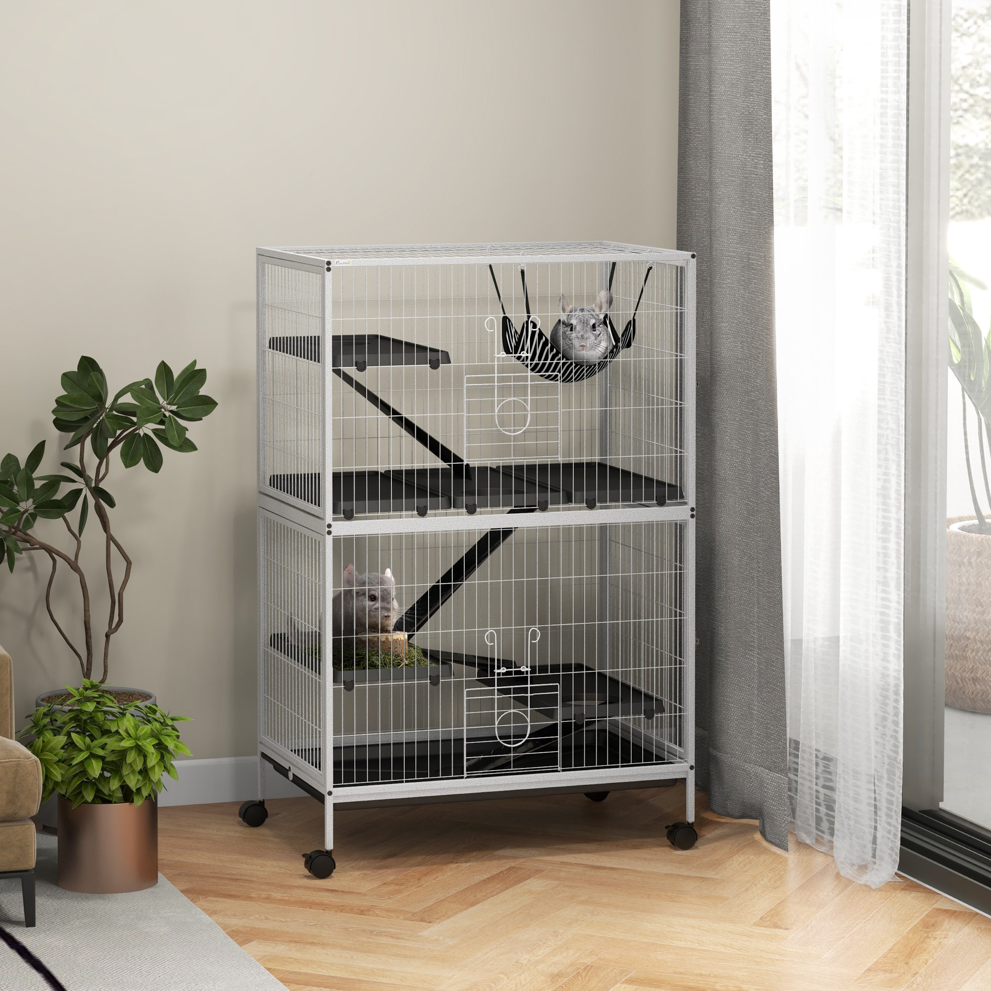 Una jaula de chinchilla de dos pisos. Hay dos chinchillas dentro. Hay plantas cerca y una ventana con cortinas.