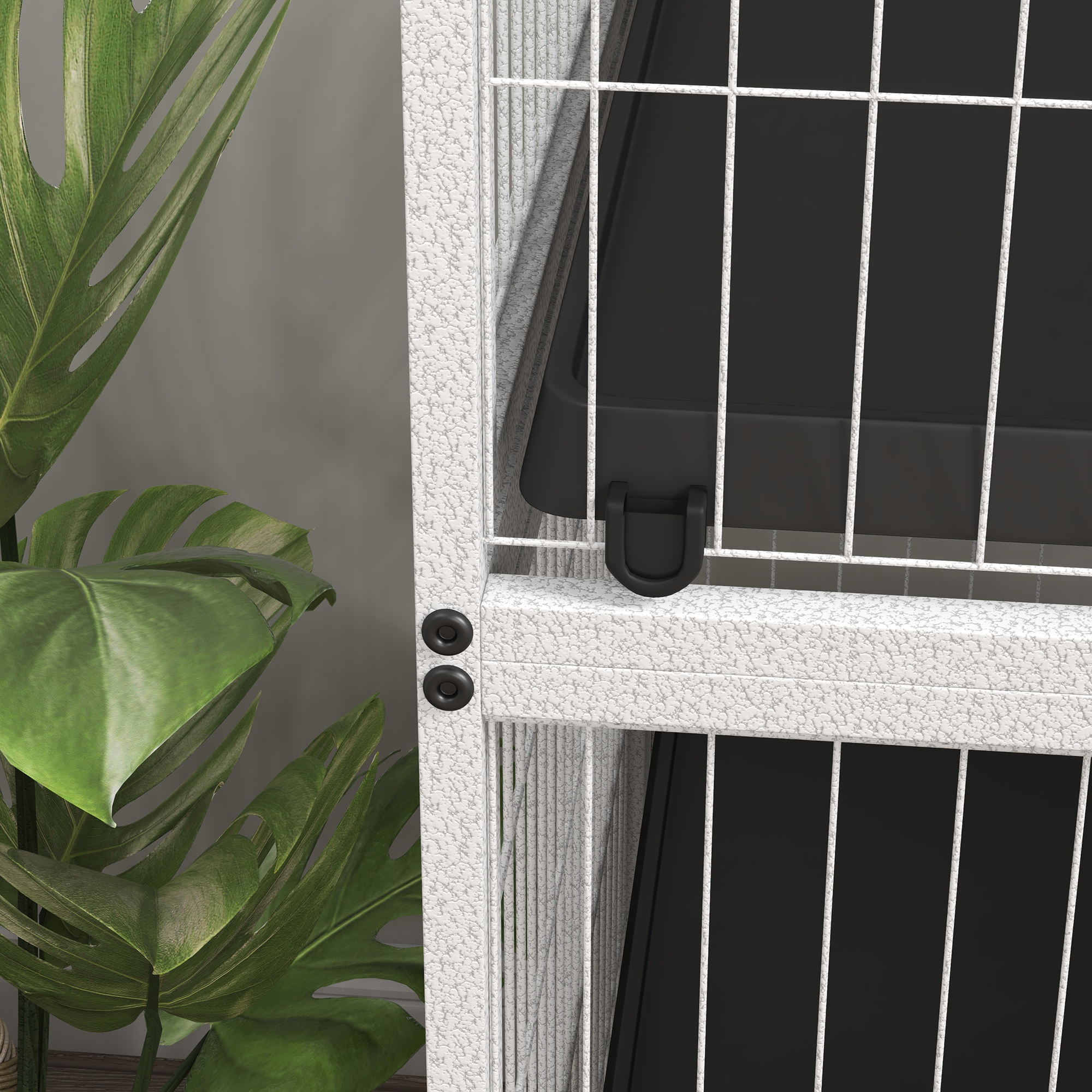 Una jaula de metal blanco con interior negro, junto a una gran planta verde con hojas texturizadas. Pared gris al fondo.