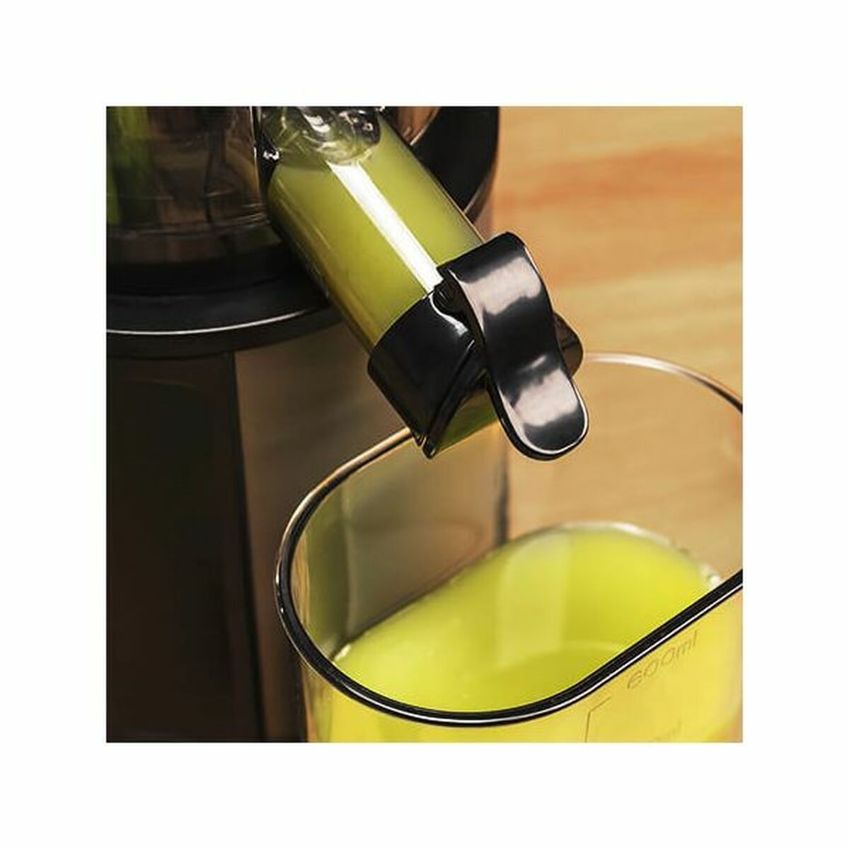 Centrifuga che eroga succo verde in un bicchiere. La centrifuga è nera con un tubo trasparente. Il bicchiere ha segni da 600 ml.