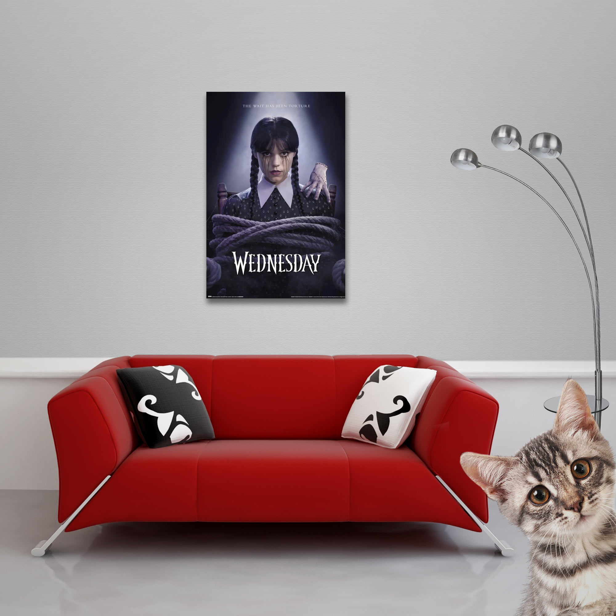 Ein Poster von Wednesday hängt über einem roten Sofa mit Kissen. Eine Katze schaut in die Ecke.