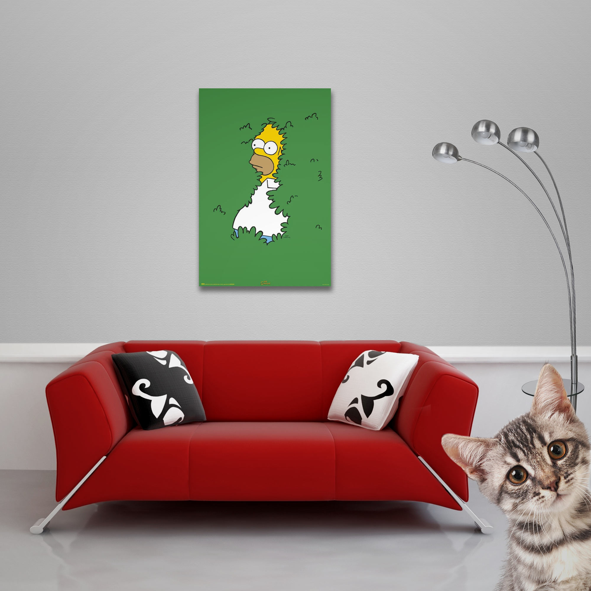 Rotes Sofa mit Kissen. Ein Bild von Homer Simpson in Büschen. Eine Katze schaut hervor. Rechts eine silberne Lampe.