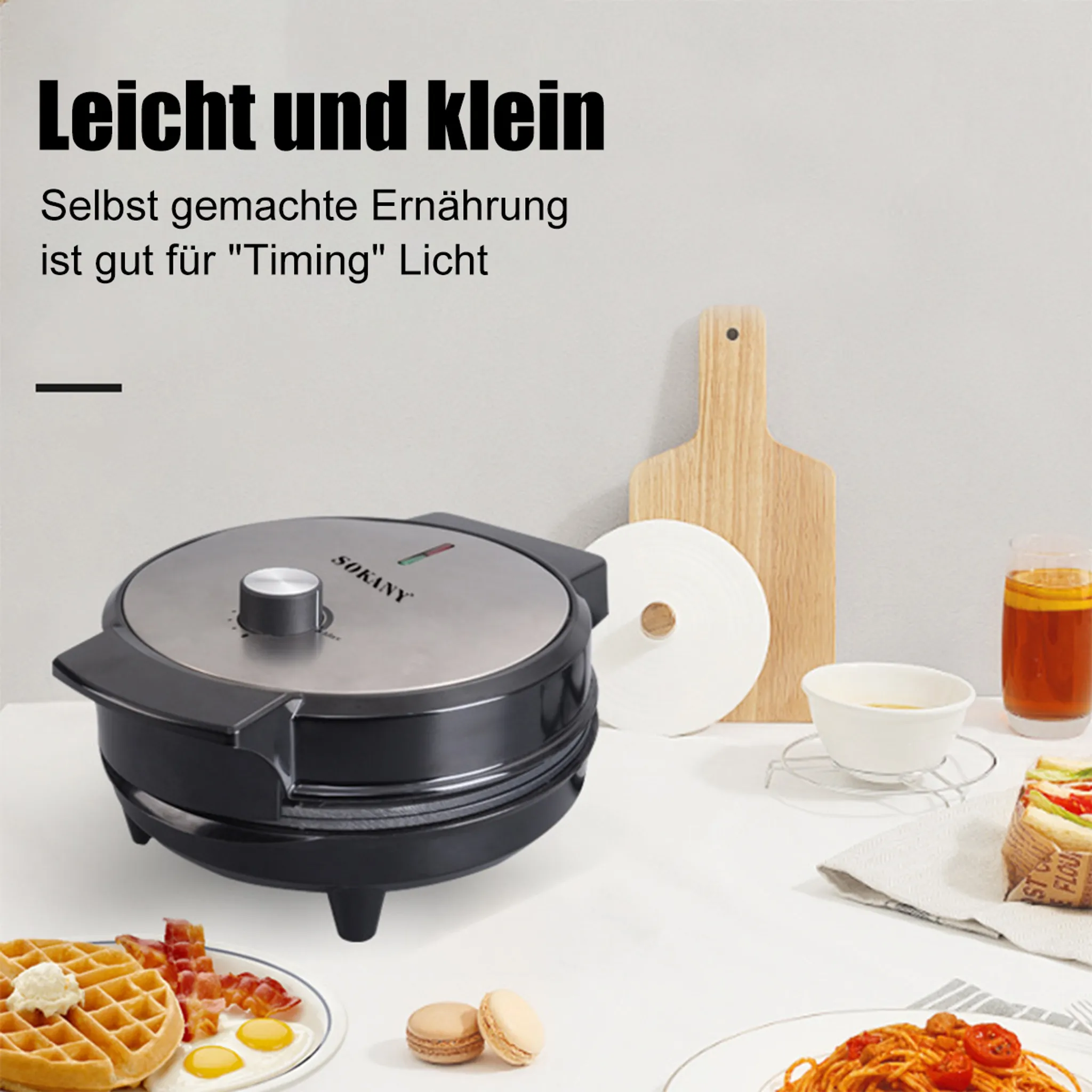 Ein Waffeleisen, Waffeln, Speck, Eier, Makronen, Pasta, ein Getränk und ein Schneidebrett stehen auf einem Tisch.