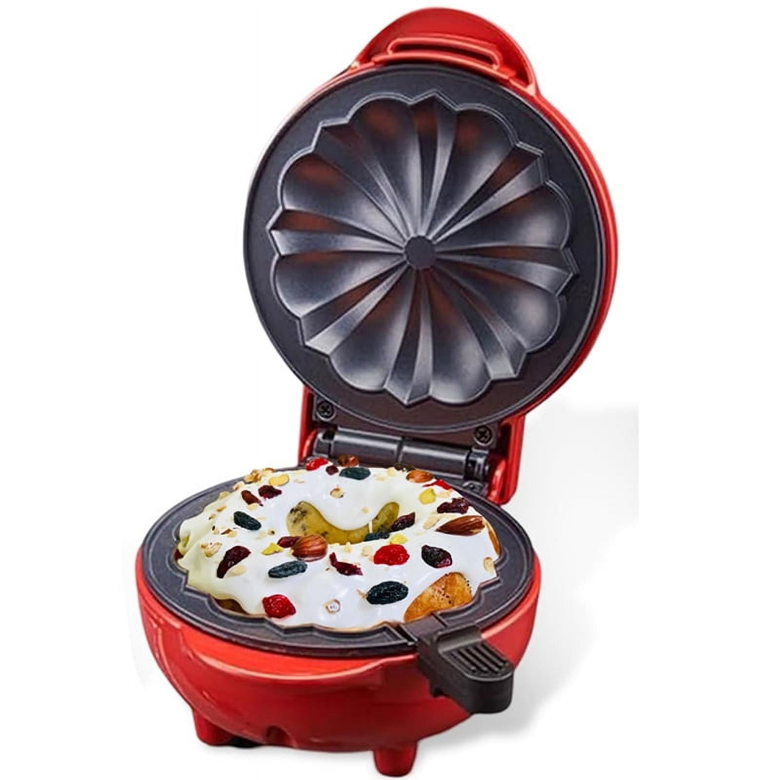 Ein roter Gugelhupf-Maker mit einem dekorierten Kuchen darin. Der Deckel ist offen. Der Kuchen ist mit Nüssen und Früchten belegt.