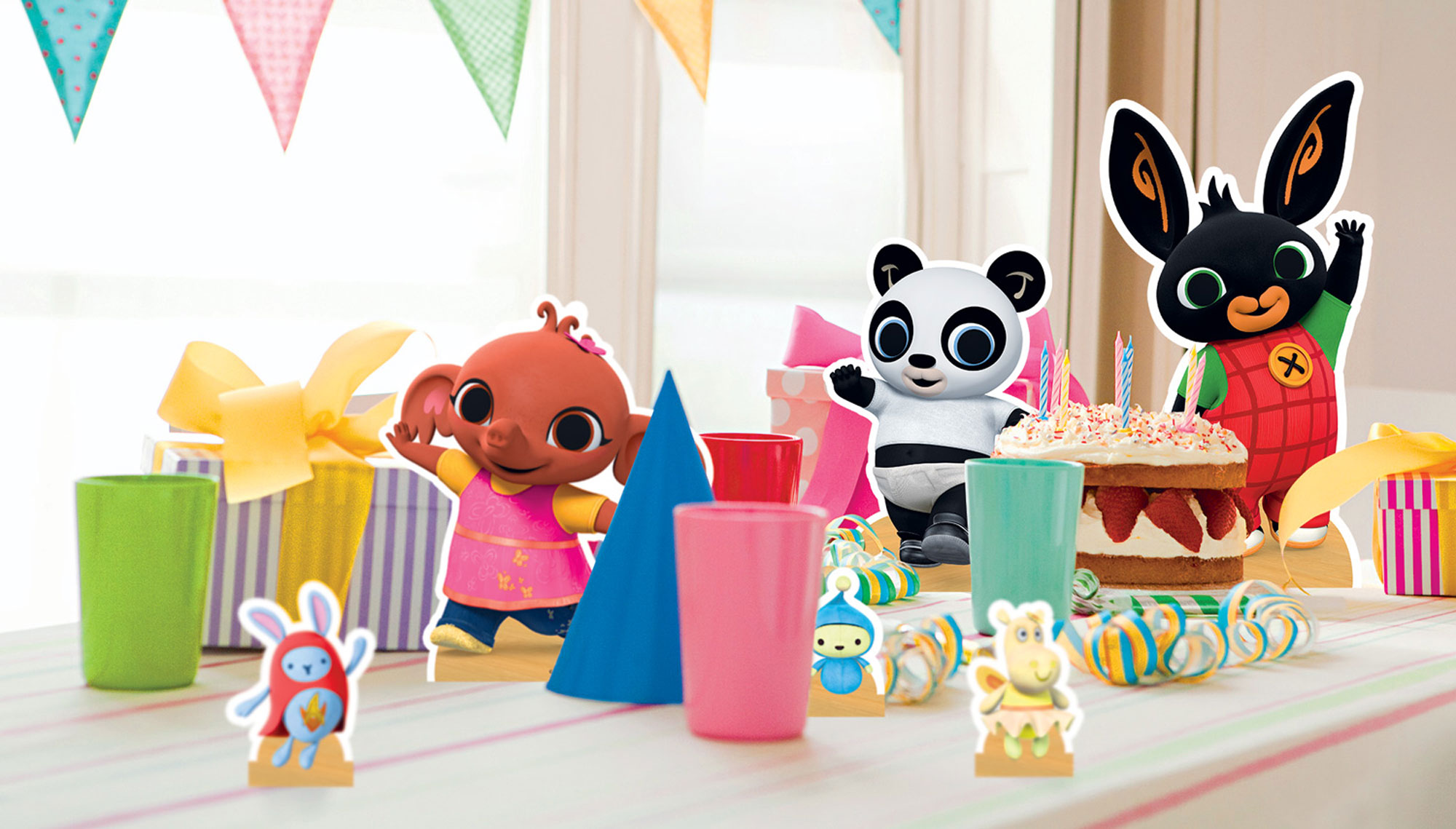 Eine Partyszene mit Zeichentrickfiguren: ein Elefant, ein Panda und ein Hase. Ein Kuchen, Geschenke und bunte Dekorationen sind vorhanden.