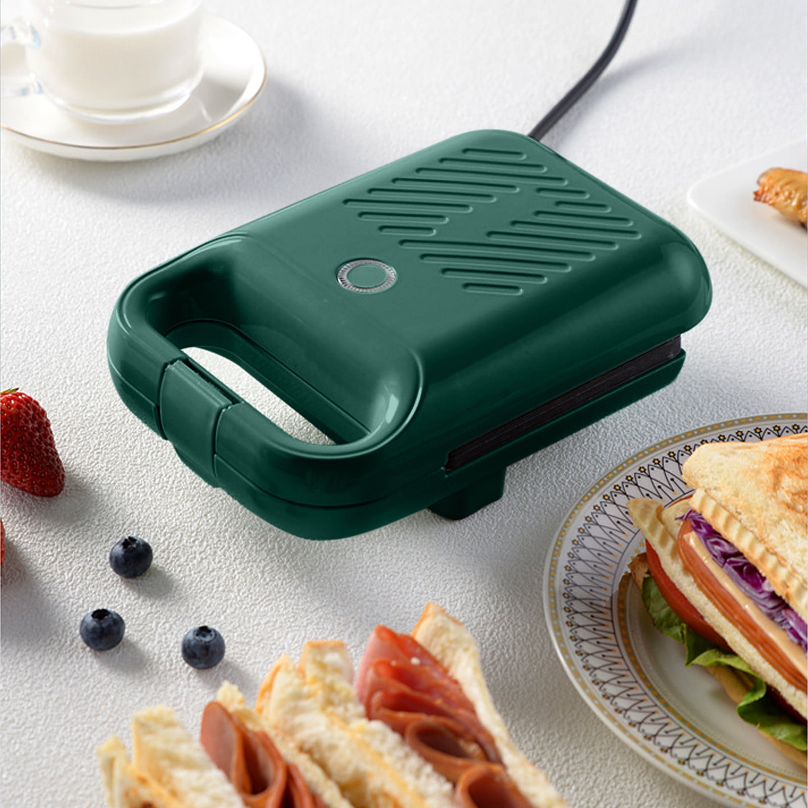 Grüner Sandwichmaker auf weißer Oberfläche, mit Sandwich, Früchten und einem Glas Milch.