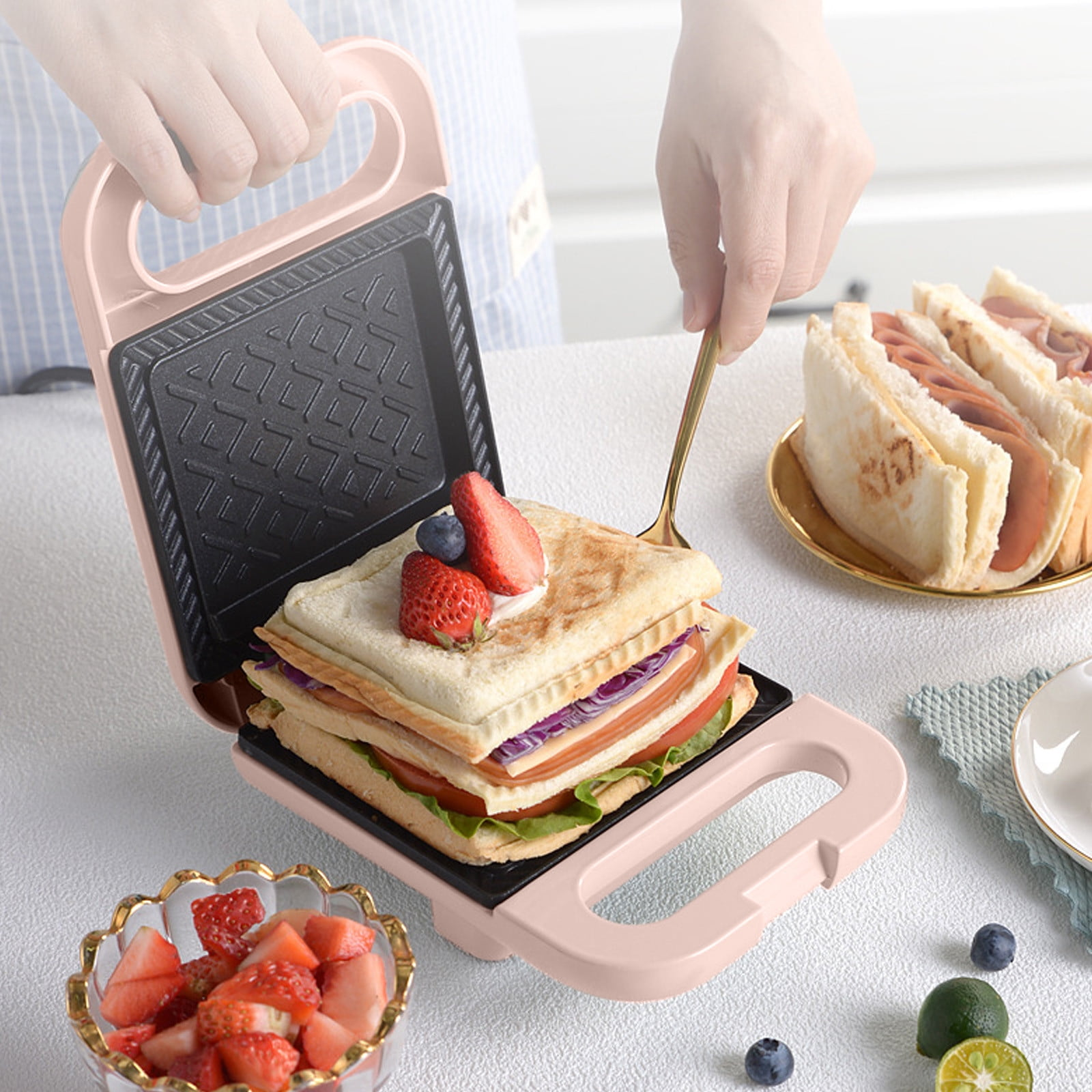 Sandwichmaker mit Sandwich. Erdbeeren und Blaubeeren oben. Weitere Sandwiches auf einem Teller.