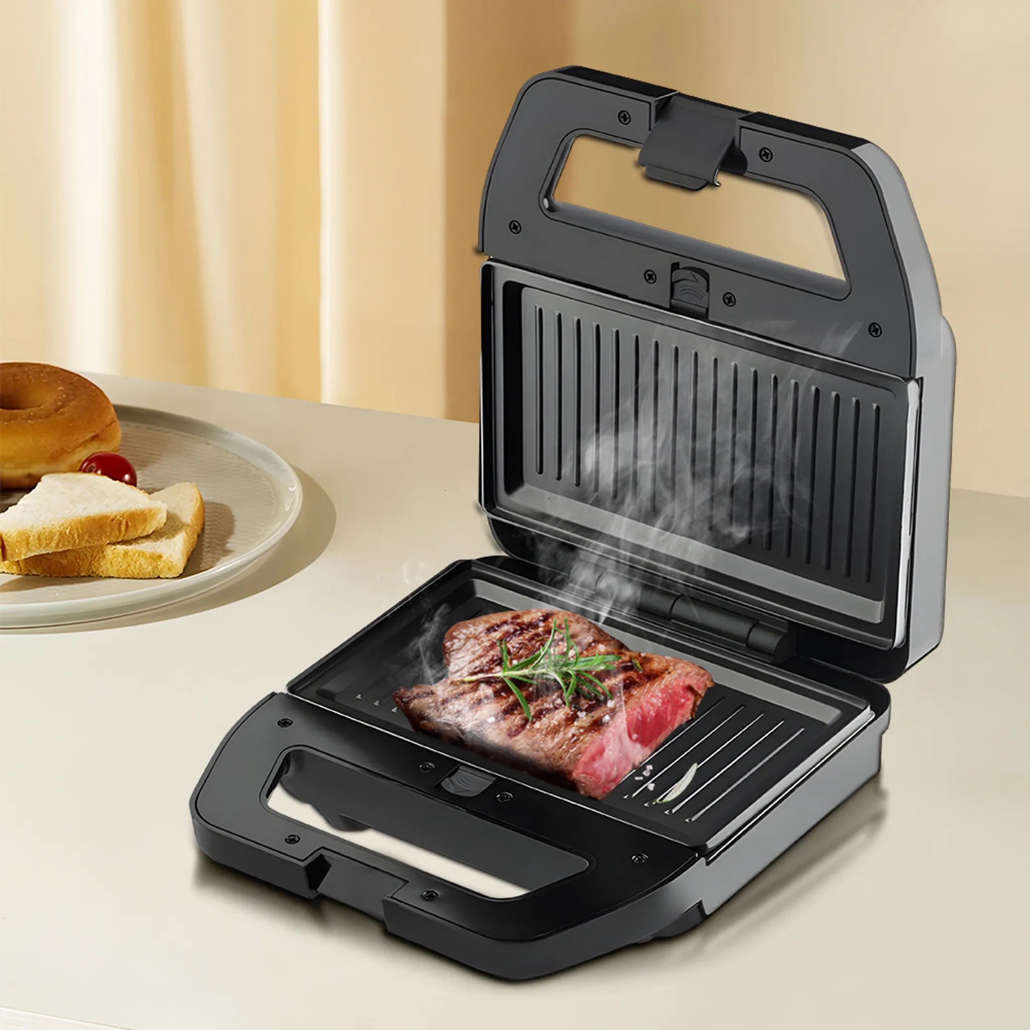 Offener schwarzer Sandwichmaker mit Steak, Dampf und Rosmarin. Brot und ein Donut befinden sich auf einem Teller im Hintergrund.