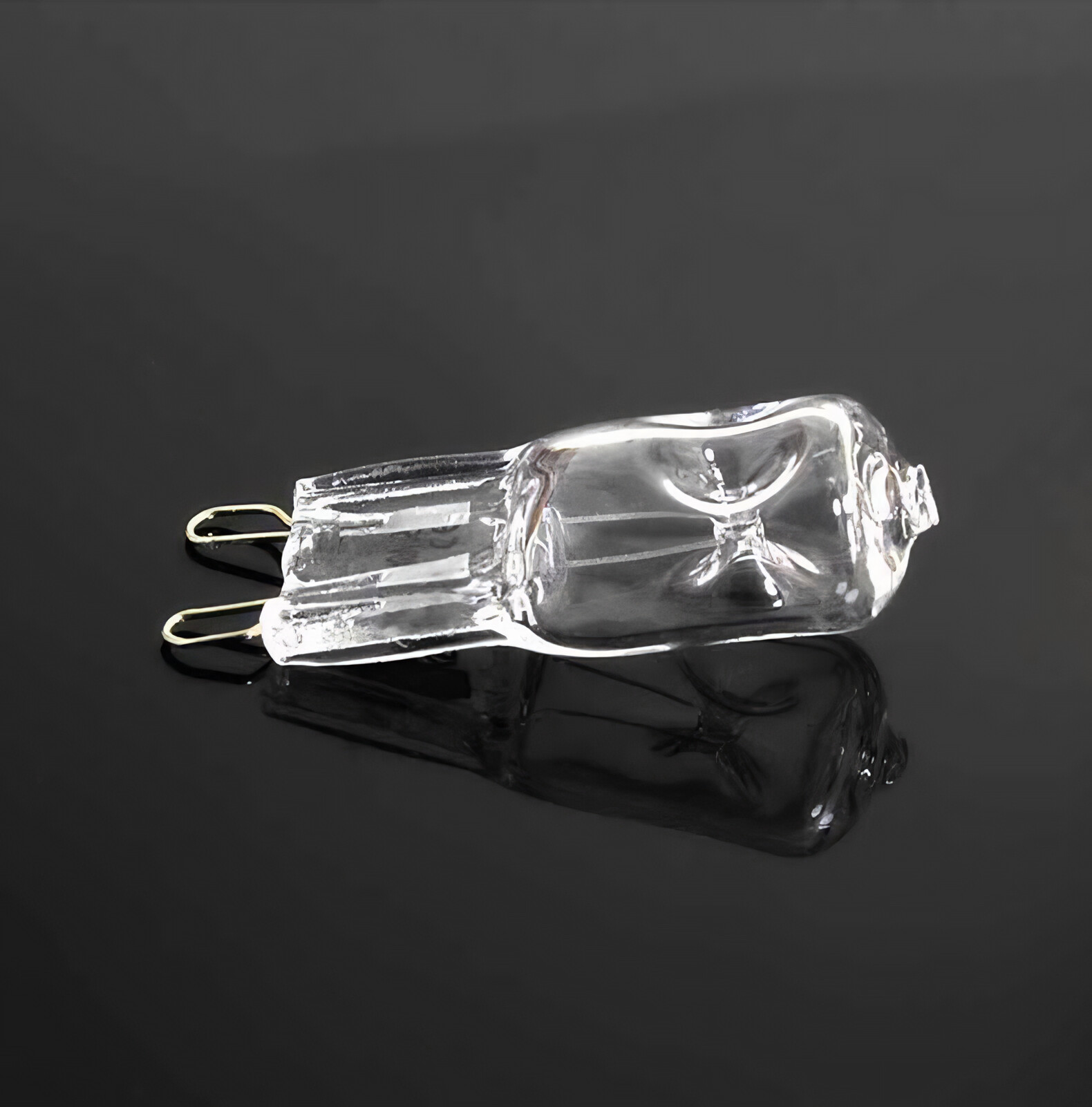Eine klare Halogenlampe mit Goldstiften auf einer reflektierenden schwarzen Oberfläche. Die Glühbirne liegt horizontal.