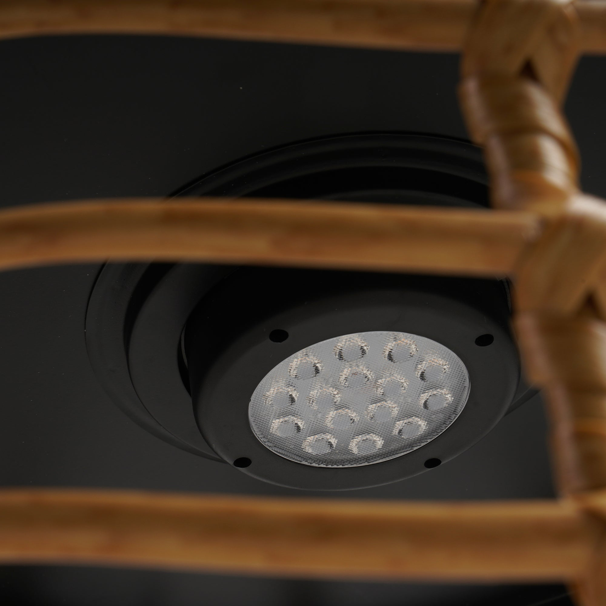 Nahaufnahme einer schwarzen Einbauleuchte mit einem Raster von LEDs, durch einen gewebten Rattanschatten betrachtet.