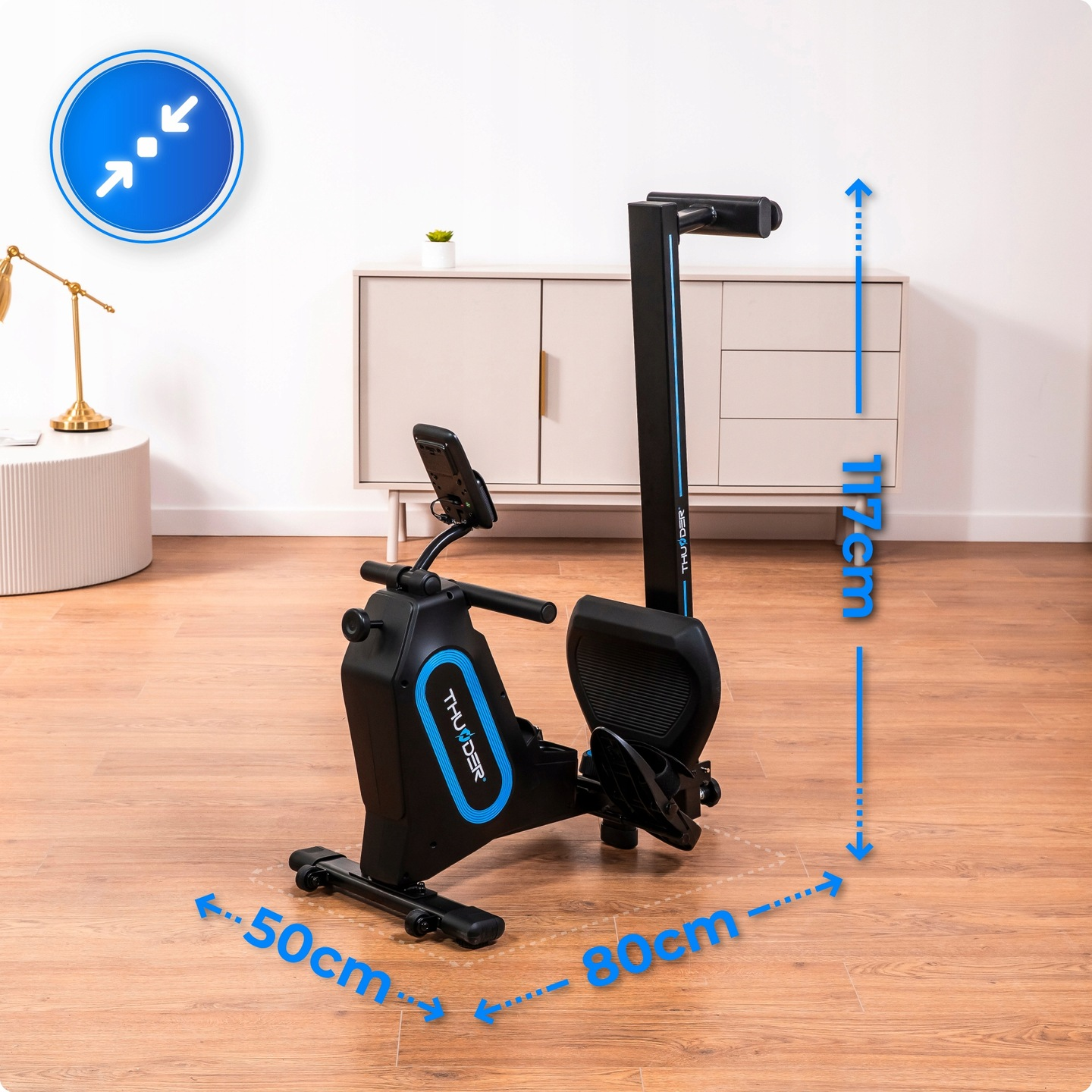 Czarna maszyna do wiosłowania z niebieskimi akcentami. Wymiary: 117cm wys., 80cm dł., 50cm szer. Tło: biała ściana i szafka.