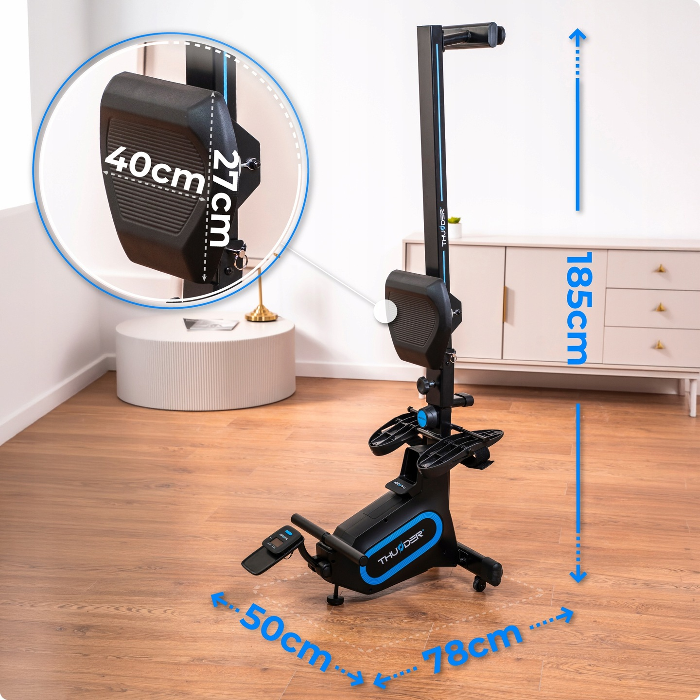 Czarna maszyna do wiosłowania z niebieskimi akcentami, oznaczone wymiary. Tło: biała ściana, szafka i drewniana podłoga.