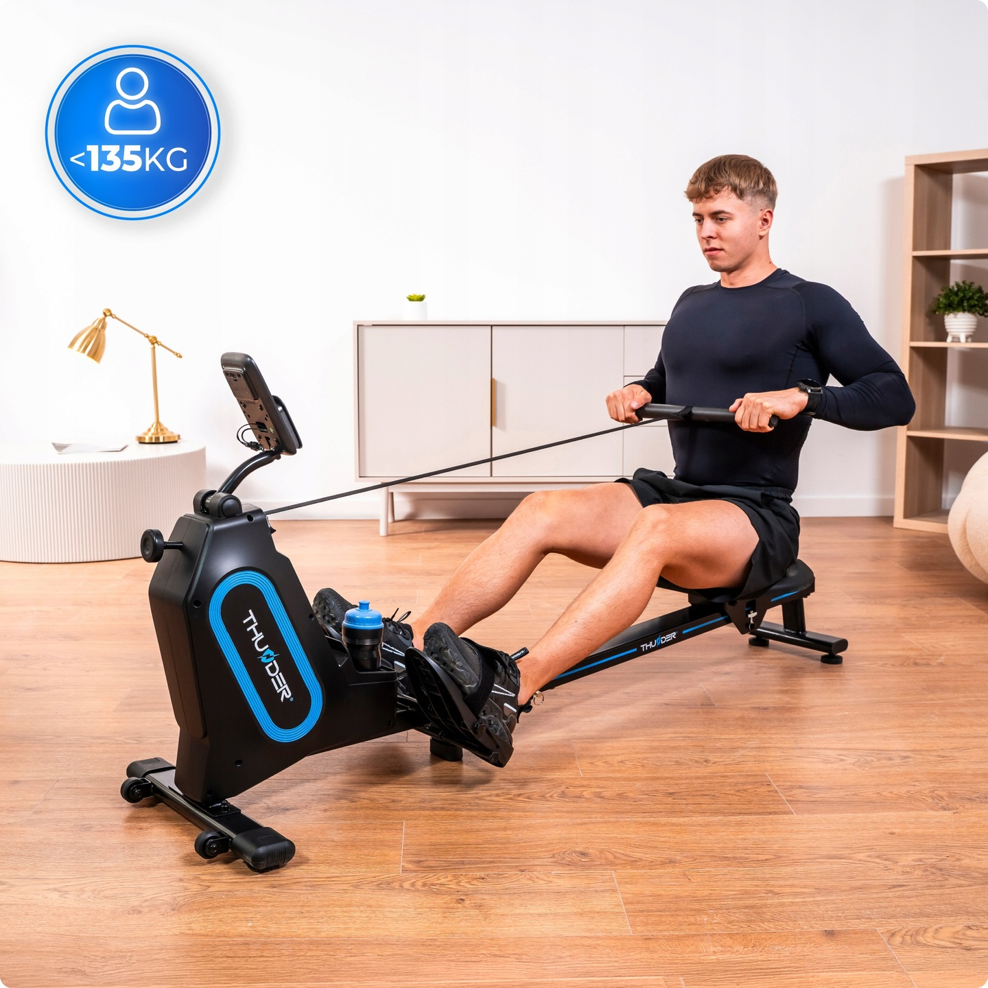 Mężczyzna wiosłuje na maszynie. Maszyna jest czarna i niebieska. W lewym górnym rogu znajduje się naklejka z limitem wagi.