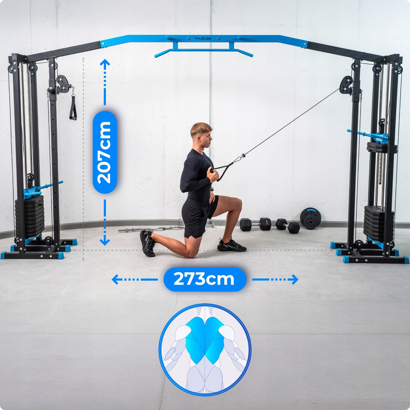 Mężczyzna ćwiczący na maszynie linowej. Maszyna jest czarno-niebieska. Ciężary, hantle leżą na podłodze. Widoczne są wymiary.