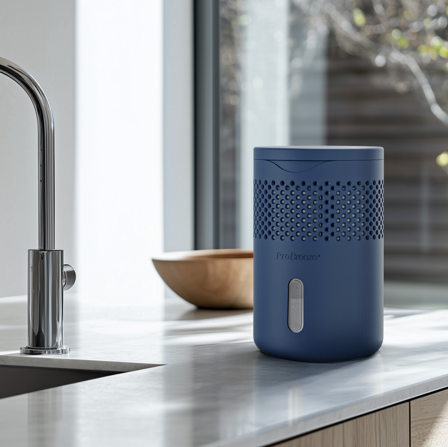 Ein marineblauer Luftreiniger steht auf einer weißen Arbeitsplatte. Links ist ein verchromter Wasserhahn. Im Hintergrund eine Holzschüssel.